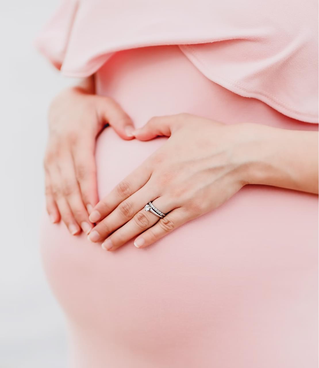 Беременная девушка показывает сердечко руками возле живота